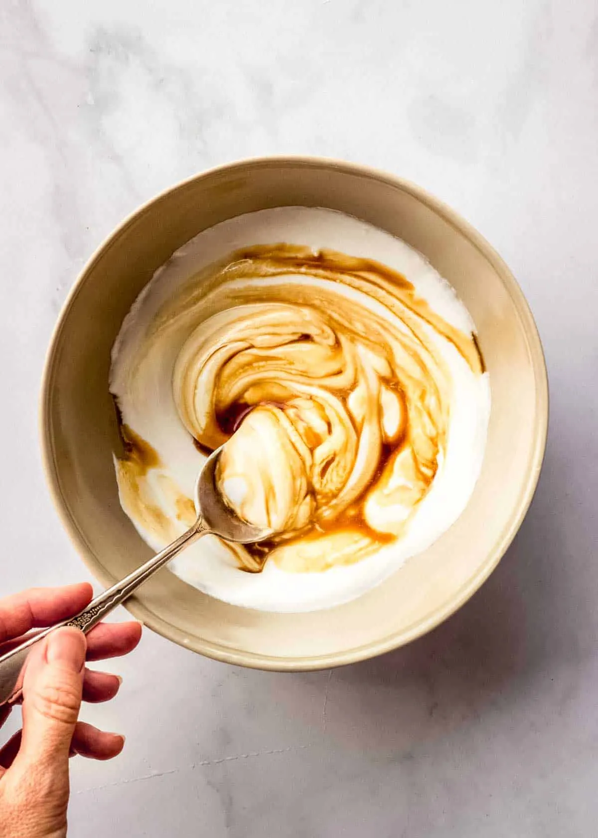 Eine Frau rührt eine braune Schüssel mit Kokosjoghurt, Ahornsirup und Vanilleextrakt.