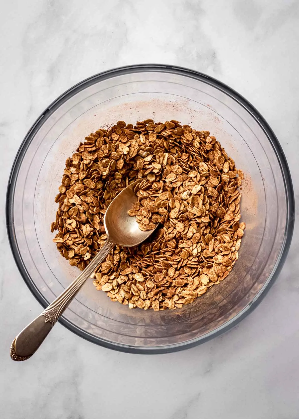 Eine große Glasschüssel mit Haferflocken, Kakaopulver und Chiasamen mit einem Metalllöffel.
