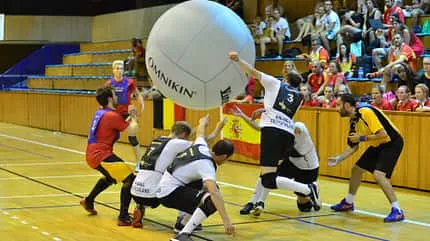 Eine Gruppe Männer spielt in einer Sporthalle mit einem großen Ball, der in die Luft geschlagen wird.