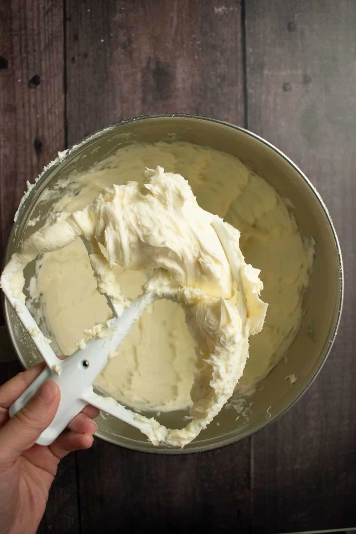 Eine Hand hält das Rührelement einer Küchenmaschine mit Buttercreme daran.