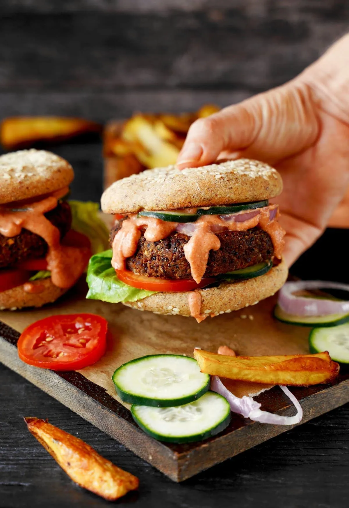 Eine Hand hält einen herzhaften Quinoa-Linsen-Veggie-Burger, reich an pflanzlichem Eiweiß und Ballaststoffen, ein gesundes veganes Mittagessen.