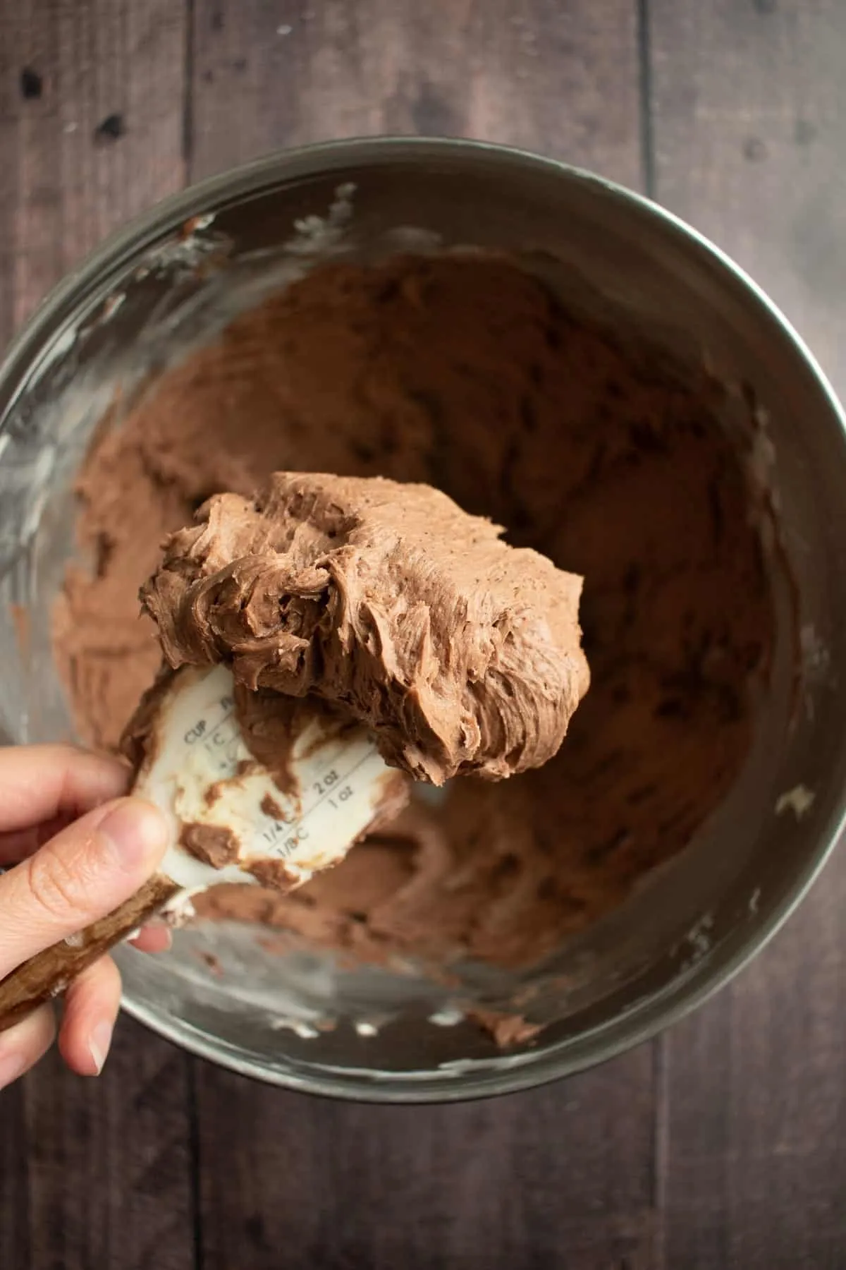 Eine Hand hält einen Silikonspatel mit fluffigem Schokoladenfrosting darauf.