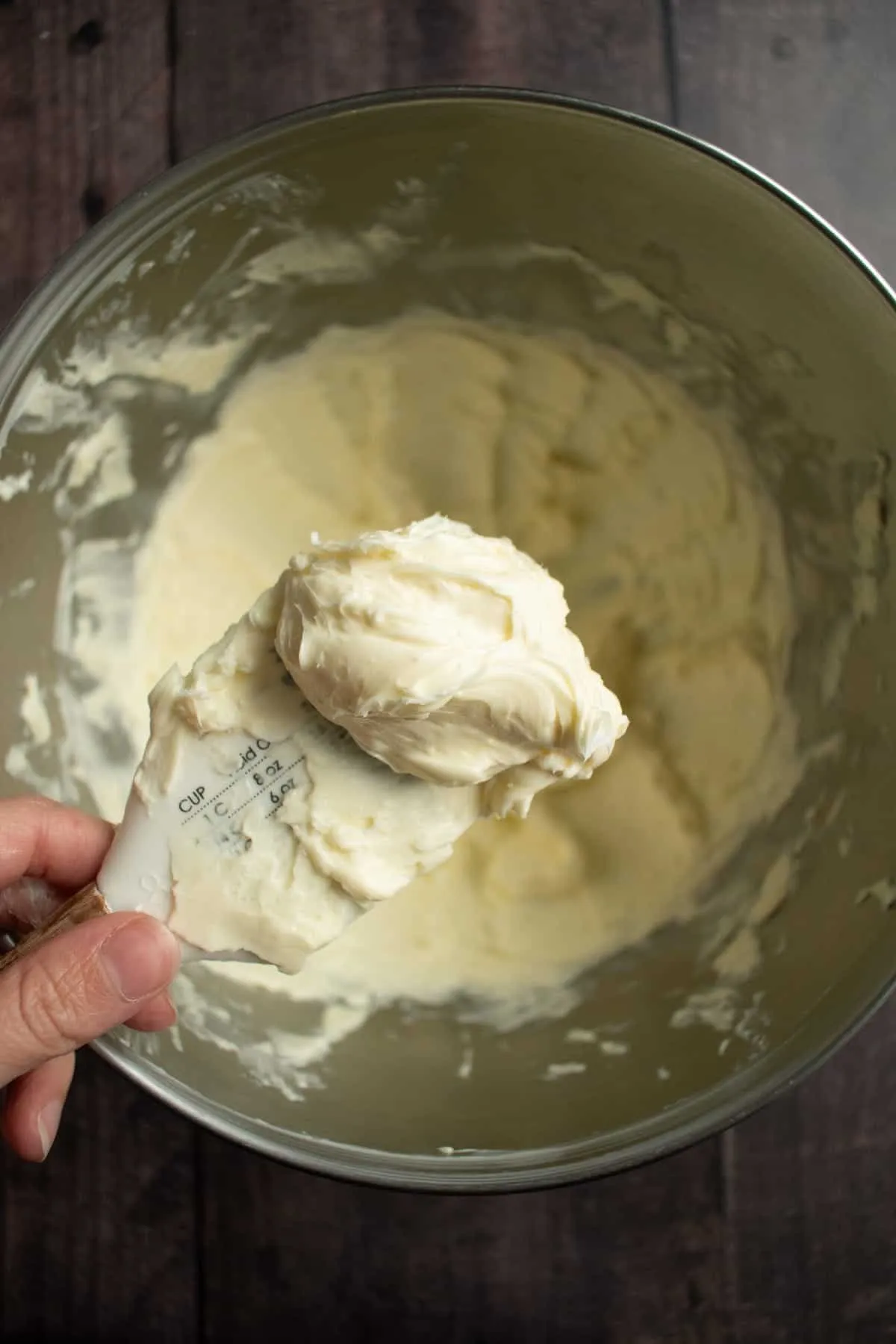 Eine Hand hält einen Spatel mit leichter, aufgeschlagener Butter über einer Rührschüssel.