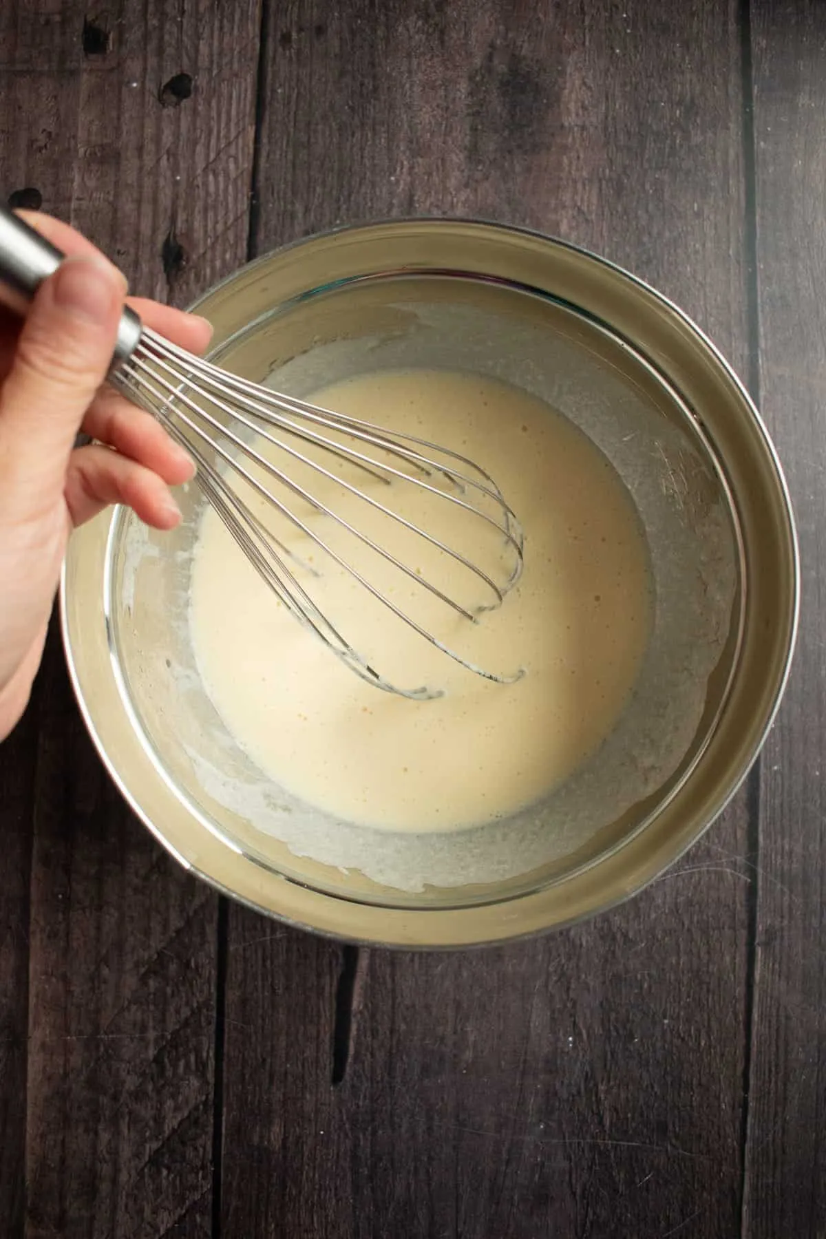 Eine Hand rührt griechischen Joghurt, Eier und Pflanzenöl in einer Metallschüssel.