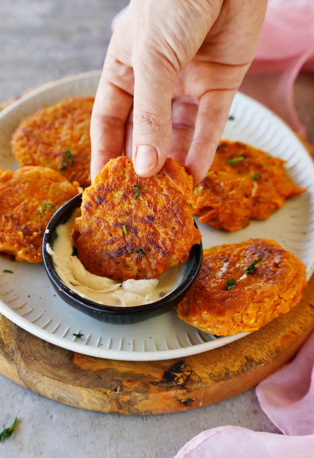 Eine Hand taucht einen Karotten-Puffer in eine cremige Soße, ideal als Snack