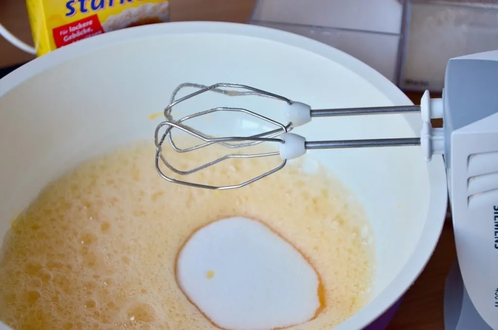 Eine Küchenmaschine schlägt Eier und Zucker zu einer hellen, schaumigen Masse in einer großen Rührschüssel