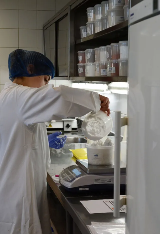 Eine Lebensmitteltechnikerin wiegt in einem Labor im Rahmen einer Lebensmittelanalyse Pulver auf einer Waage ab.