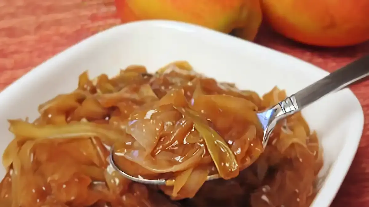 Eine Löffelportion karamellisierter Schmorkohl, serviert aus einer weißen Schüssel, mit Äpfeln im Hintergrund.