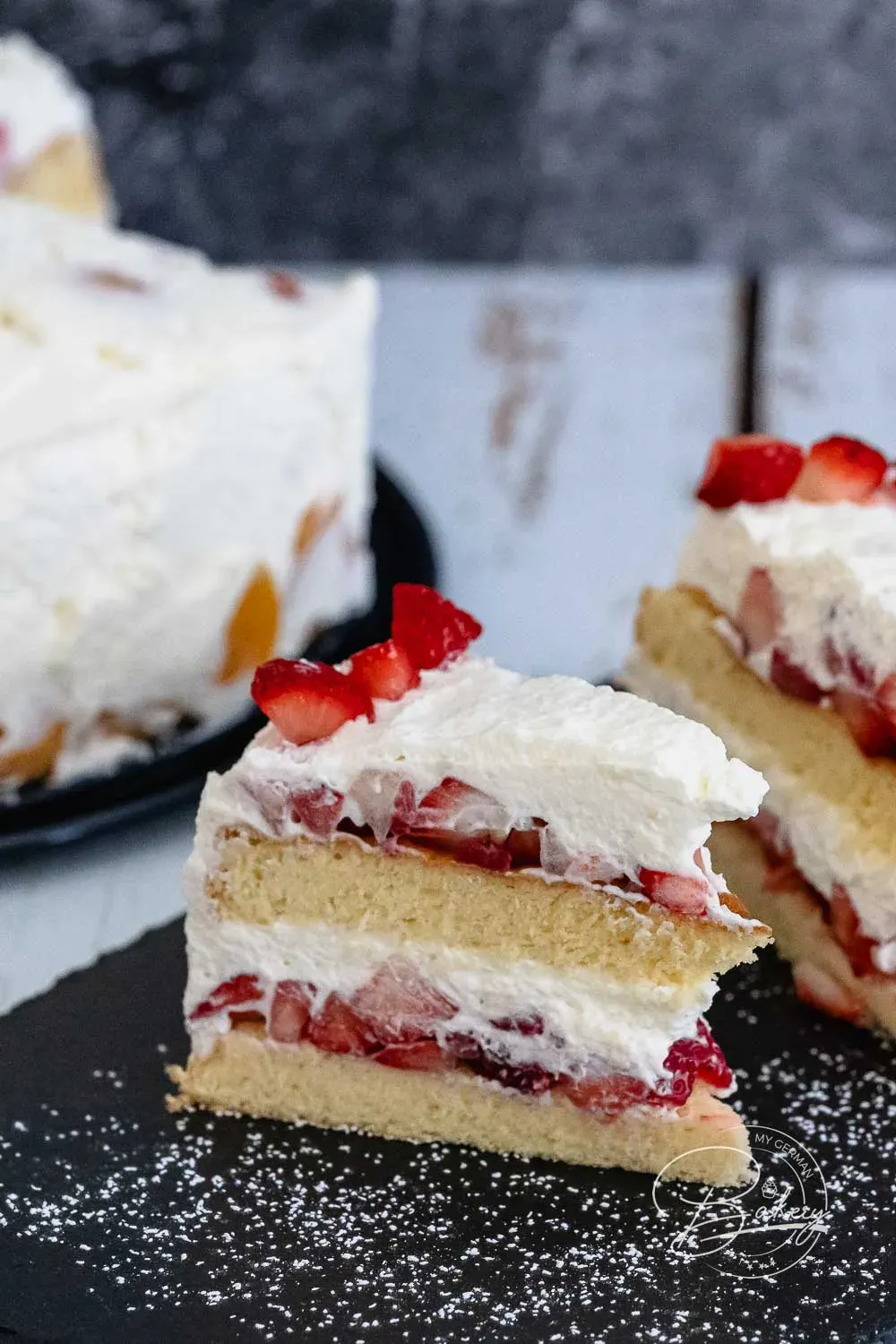 Eine Nahaufnahme der Schichtung einer Erdbeer-Sahne-Torte, bei der frische Erdbeeren und geschlagene Sahne auf dem Biskuitboden verteilt werden.