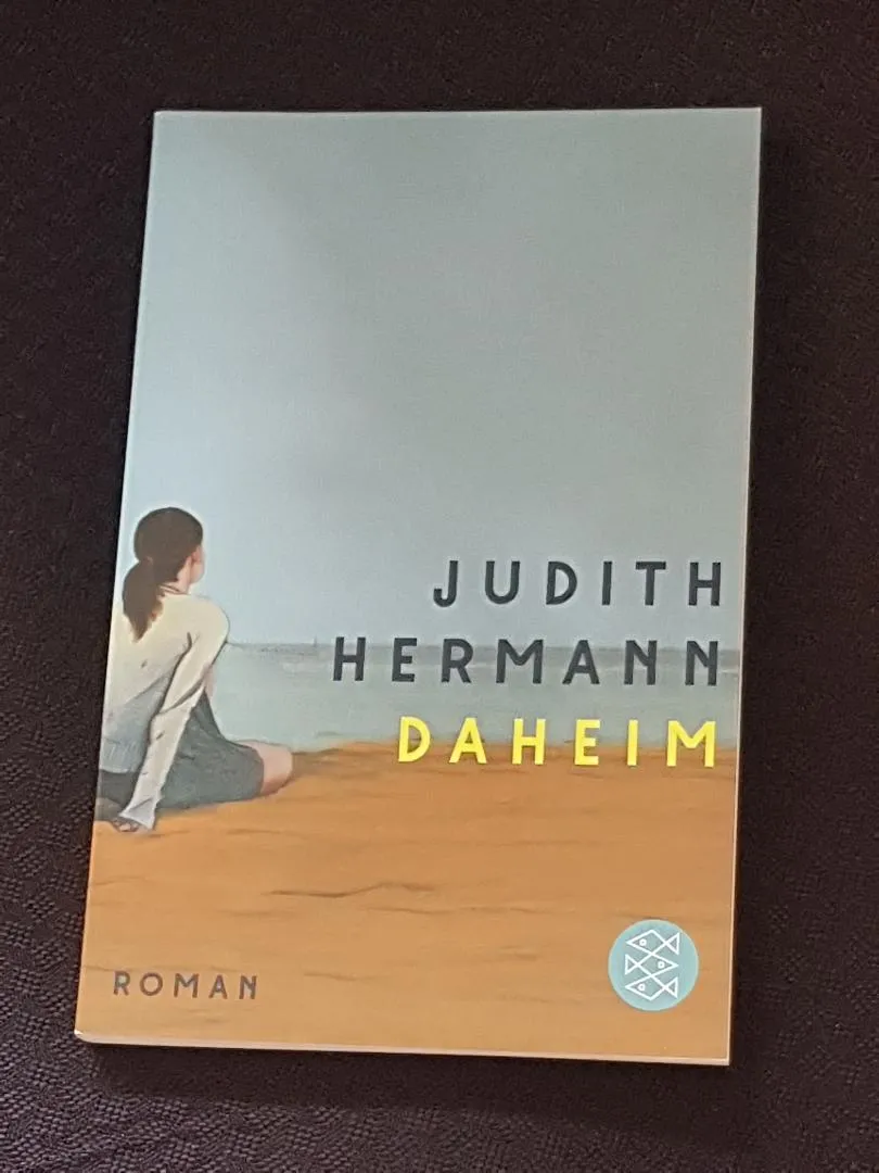 Eine Nahaufnahme des Covers von Judith Hermanns Roman "Daheim" mit einem minimalistischen Design in dunklen Tönen, das die melancholische und introspektive Stimmung des Buches einfängt.