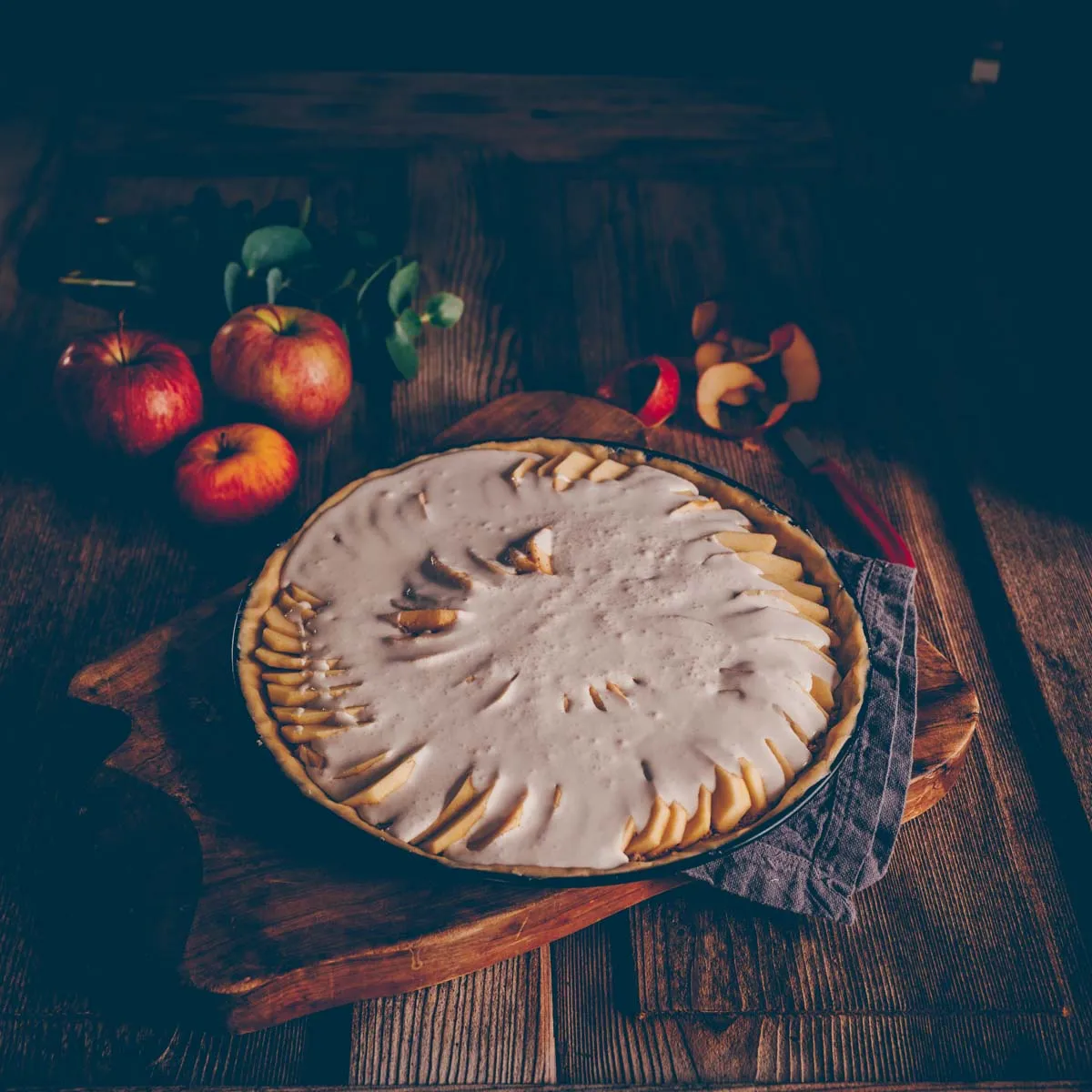 Eine Nahaufnahme des Gusses, der über die angeordneten Apfelscheiben auf dem Wähenboden gegossen wird.