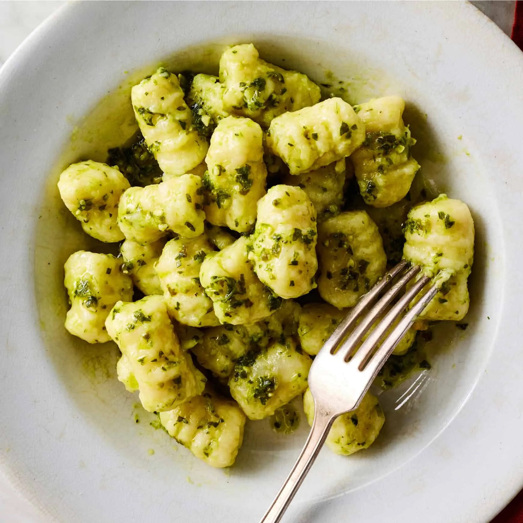 Eine Nahaufnahme von perfekt zubereiteten Gnocchi mit einer leichten Soße und Basilikumgarnitur.