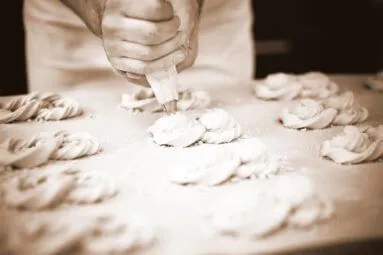 Eine Person formt mit einem Spritzbeutel elegante Teigwirbel auf einem Tablett.