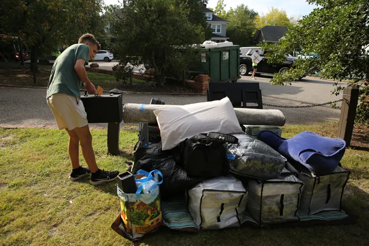 Eine Person hält eine Tasche in der Nähe von gepackten Gegenständen, bereit für den Start in ein neues Projekt.