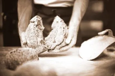 Eine Person hält einen gebrochenen Laib rustikales Brot über einen Holztisch.