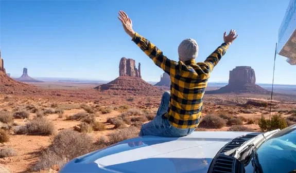 Eine Person in kariertem Hemd sitzt auf einem Auto und breitet die Arme aus