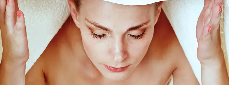 Eine Person inhaliert warmen Wasserdampf aus einer Schüssel, um die Schleimhäute bei Halsschmerzen zu befeuchten und die Durchblutung zu fördern.