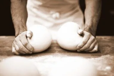 Eine Person knetet zwei Teigbällchen auf einer Holzplatte bei Theo's Bonn.