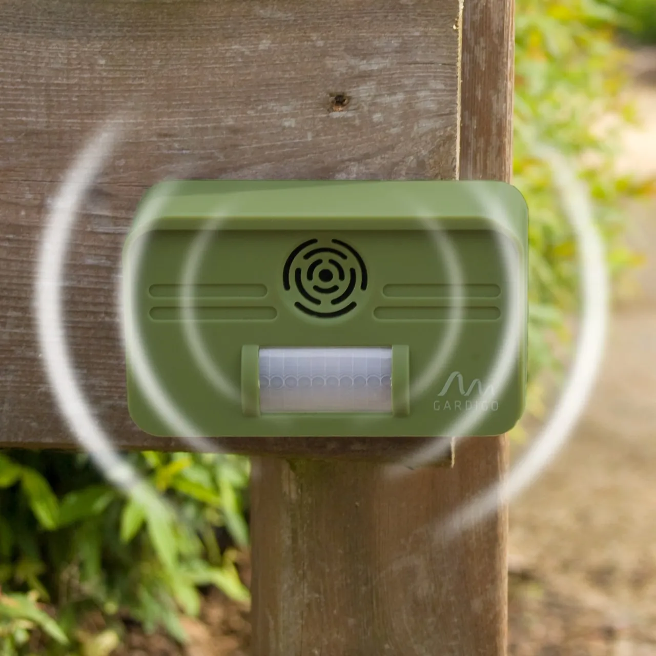 Eine Person montiert ein kleines, rechteckiges Gerät an einer Gartenmauer.