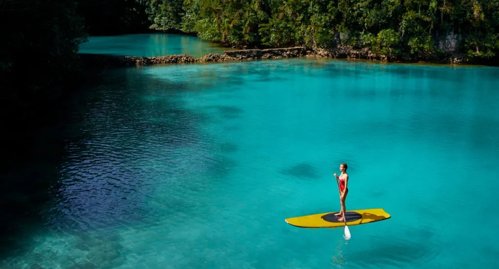 Eine Person steht auf einem Stand-Up-Paddle-Board auf einem ruhigen See im Sonnenuntergang.