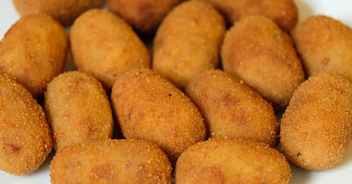 Eine Platte mit goldbraun frittierten spanischen Kroketten, einige davon halbiert, um die cremige Füllung zu zeigen, garniert mit frischer Petersilie auf einem rustikalen Teller