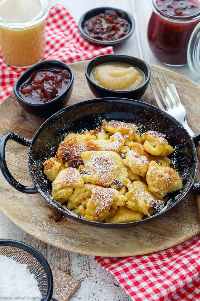 Eine Portion Kaiserschmarrn mit Zwetschgenröster und Apfelmus auf einem Holztisch.