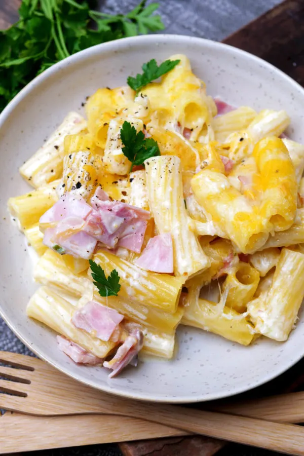 Eine Portion Nudel-Schinken-Auflauf auf einem weißen Teller, servierfertig mit cremiger Soße und goldbraunem Käse