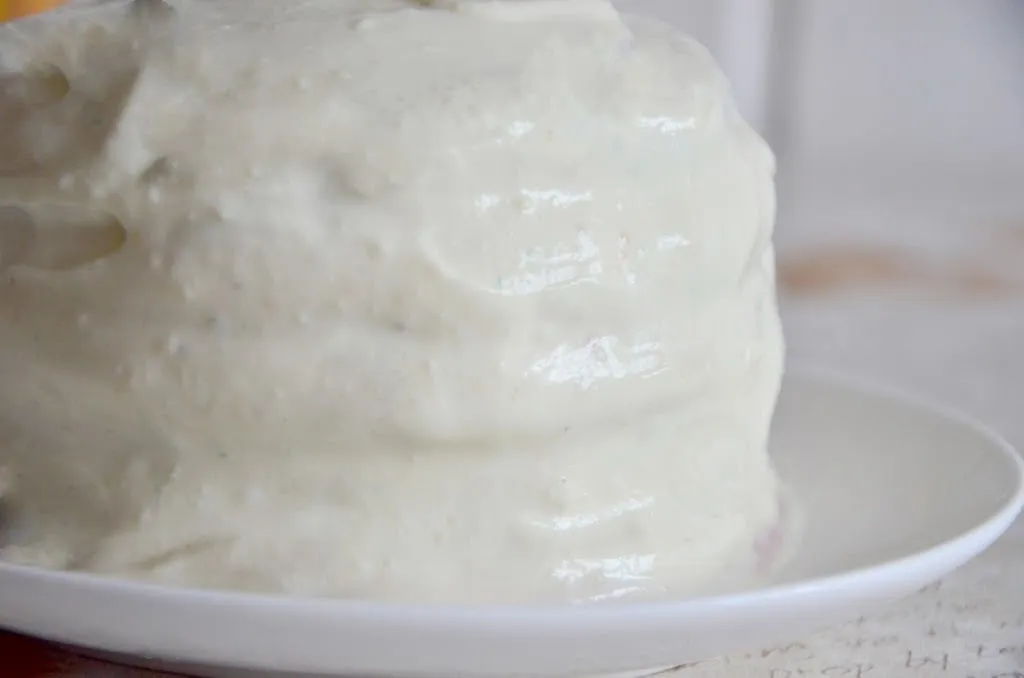 Eine Regenbogen Torte, vollständig mit weißem Frischkäse-Topping ummantelt und glatt gestrichen, wartet auf die Dekoration