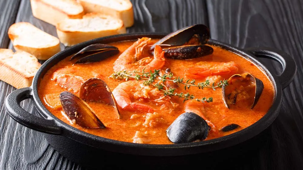 Eine reichhaltige Bouillabaisse mit verschiedenen Meeresfrüchten und Brot in einer tiefen Schale
