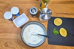 Eine Schüssel mit Crème Fraîche, Quark und den bereits zerkleinerten Zutaten, die mit einem Löffel zu einer cremigen Sour Cream verrührt werden.