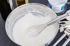 Eine Schüssel mit Joghurt, Knoblauch, Olivenöl und Essig, die verrührt werden