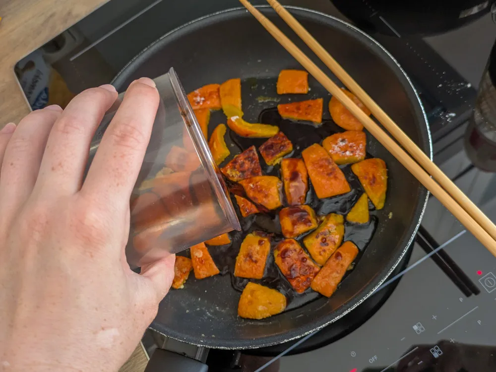 Eine süß-saure Nanbanzu-Soße wird über die angebratenen Kürbisstücke in der Pfanne gegossen.