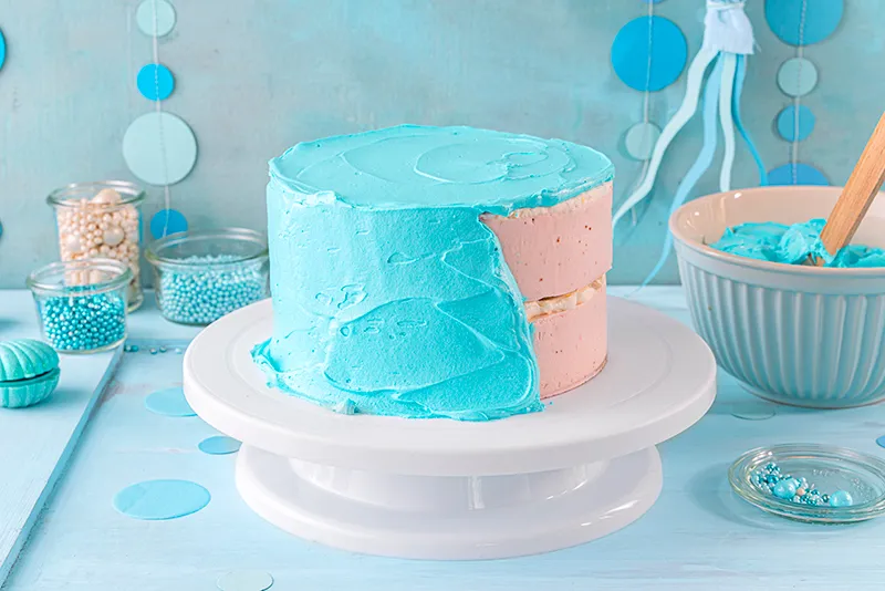 Eine Tortenpalette wird verwendet, um die blaue Schlagcreme gleichmäßig auf den Seiten der Meerjungfrauen Torte zu verteilen und zu glätten.