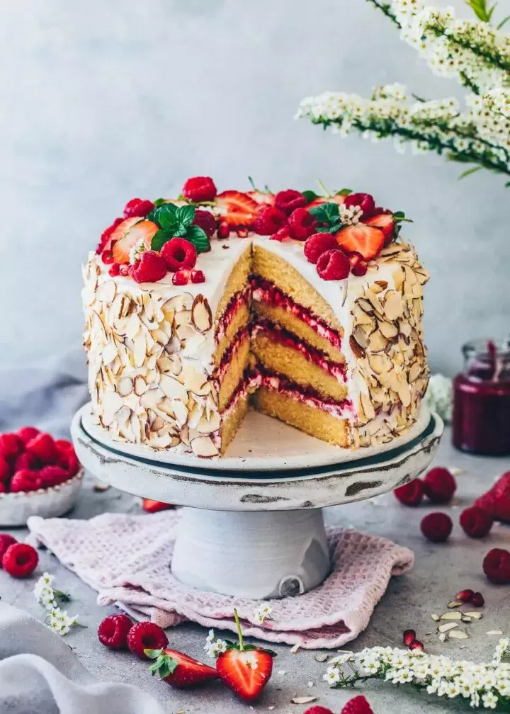 Eine vegane Himbeer-Sahne-Torte, servierfertig dekoriert mit frischen Himbeeren, Erdbeeren und Mandelblättchen