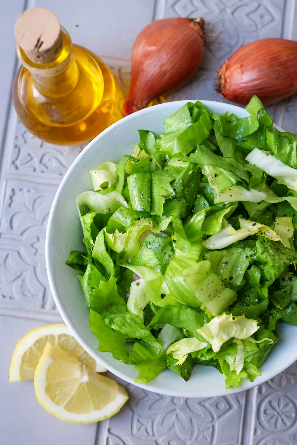 Endiviensalat auf einem Teller, umgeben von den einzelnen Zutaten des Dressings: Zitrone, Honig, Senf, Schalotte und Olivenöl.