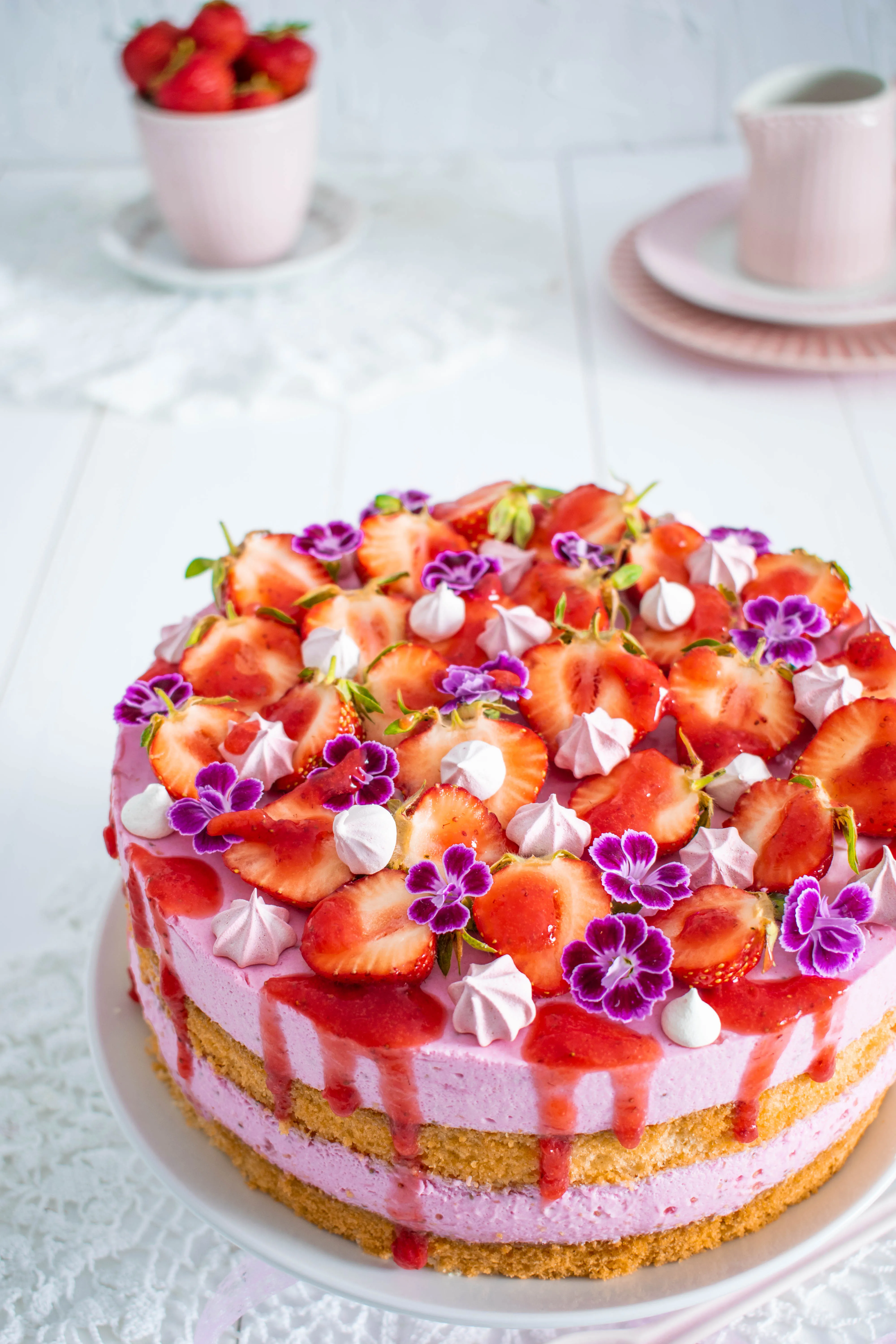 Erdbeersahnetorte von oben fotografiert, mit sorgfältig arrangierten Erdbeeren, Baiserstückchen und Blüten