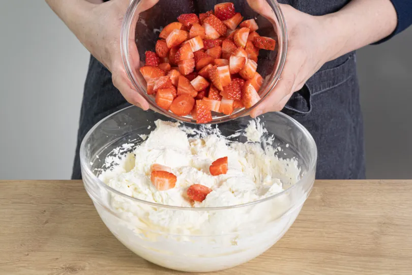 Erdbeerwürfel werden behutsam unter die lockere Frischkäse-Sahne-Creme gehoben.