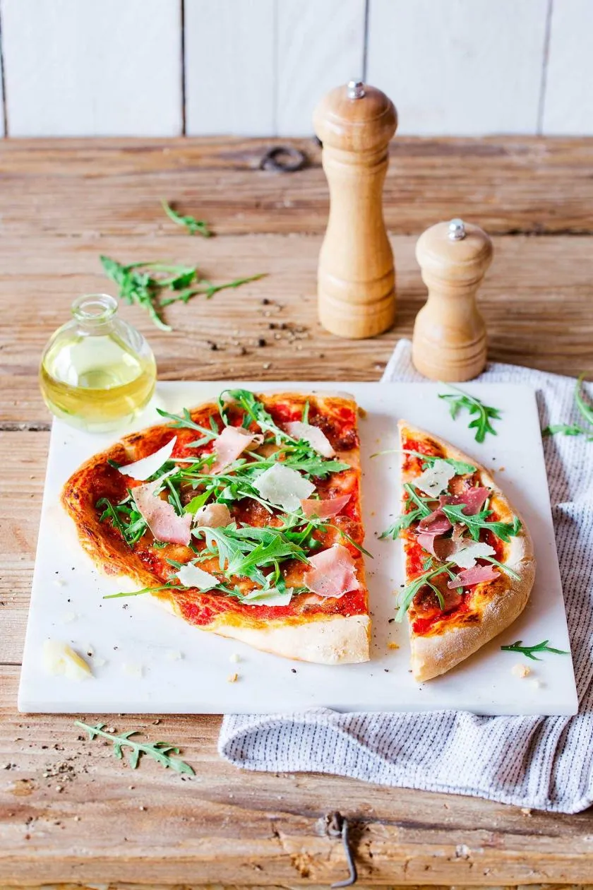 Exquisite Pizza Parma mit hauchdünnem Parmaschinken, frischem Rucola und Parmesansplittern.