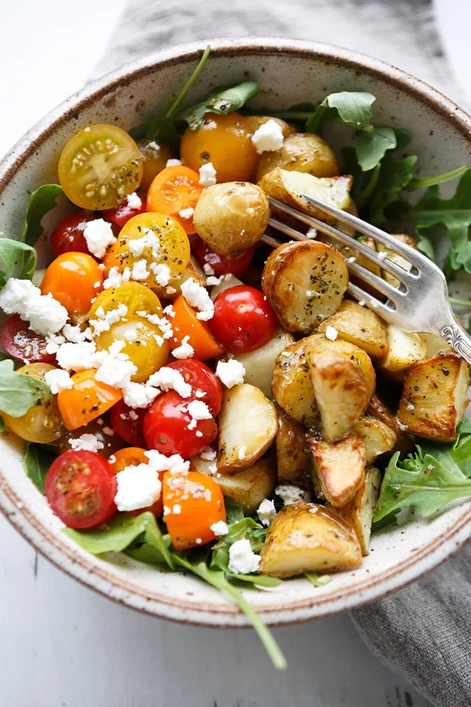 Farbenfrohe italienische Power Bowl mit gerösteten Kartoffeln, frischen Tomaten, würzigem Rucola und cremigem Feta