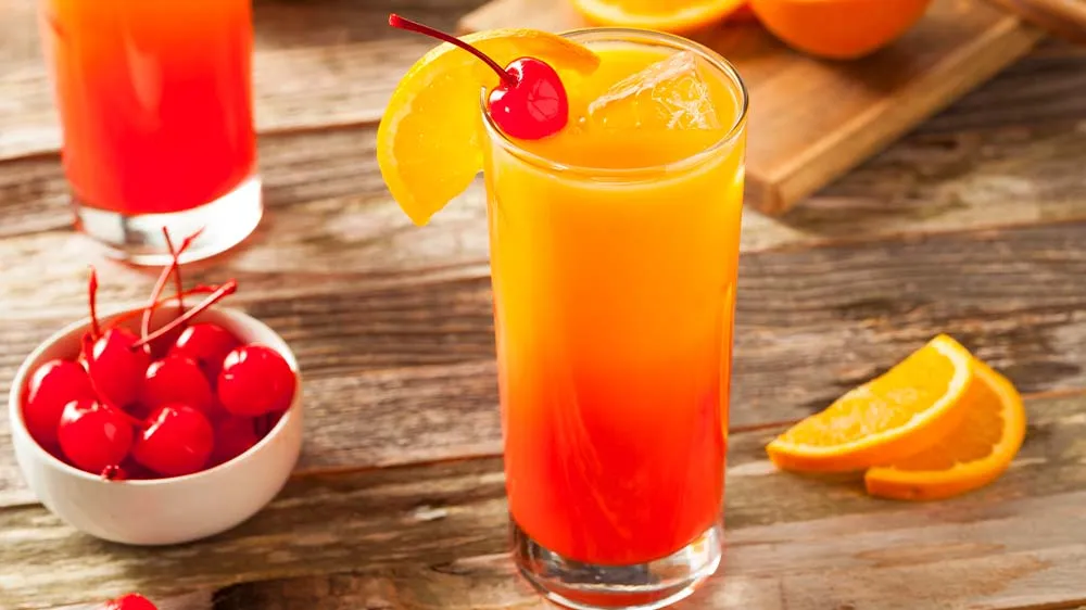 Farbenfroher Virgin Sunrise im Glas, dekoriert mit Orangenscheibe und Cocktailkirsche, Schichteffekt aus Orangensaft und Grenadine