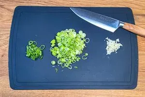 Fein gehackte Frühlingszwiebeln und Knoblauchzehen auf einem Schneidebrett, vorbereitet für die Sour Cream.
