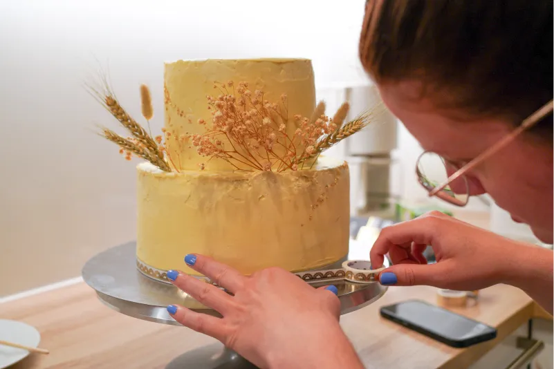 Feinarbeiten an einer Hochzeitstorte in der Nacht vor der Hochzeit, inklusive Trockenblumen und Blattgold