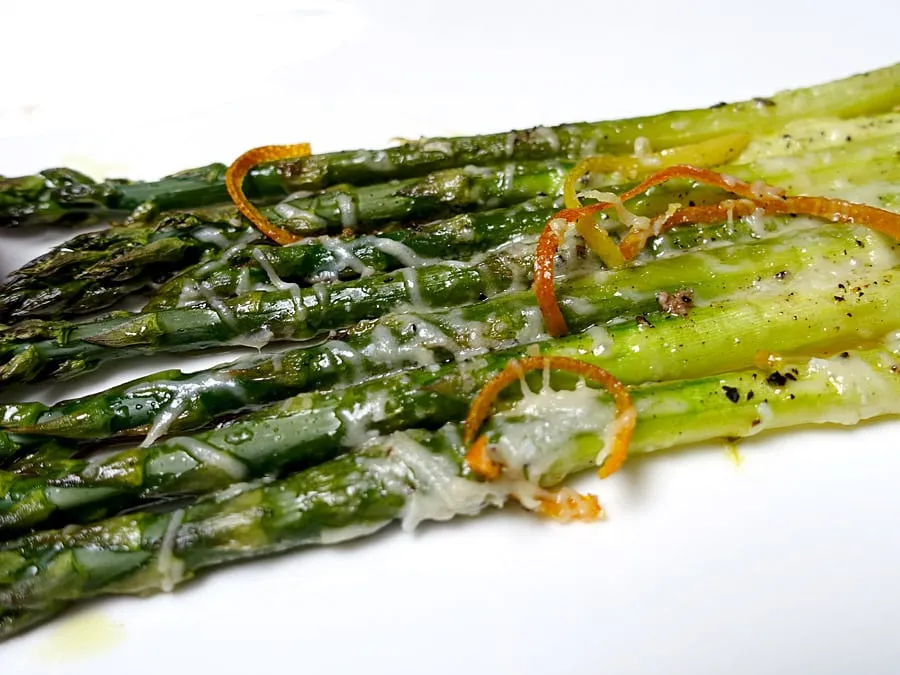 Fertig gebackener grüner Spargel mit Parmesankäse und Orangenzesten auf einem Servierteller
