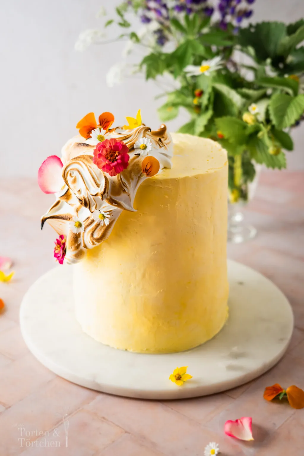 Fertige Mango Quark Sahne Torte mit samtiger Baiser-Haube und essbaren Blüten. Eine sommerliche Torte, perfekt für besondere Anlässe.