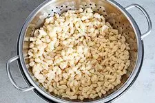 Fertige Spätzle werden in einer vorgewärmten Servierschüssel angerichtet, bereit als Beilage für ein traditionelles deutsches Gericht.