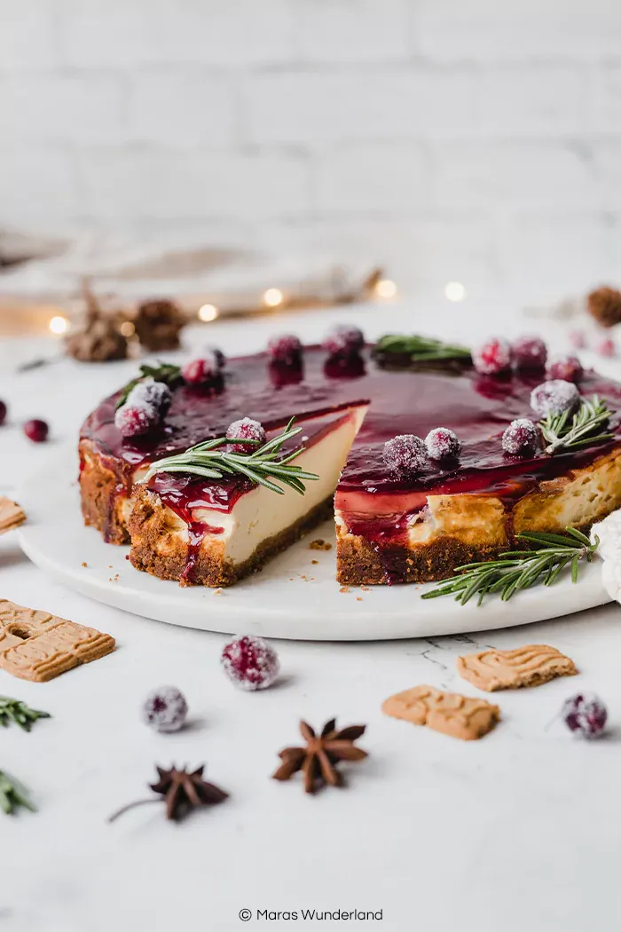 Festlicher Glühwein-Käsekuchen mit Spekulatius-Boden, verziert mit gezuckerten Cranberries und Rosmarin für die Weihnachtszeit.