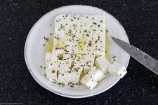 Fetakäse wird mit Olivenöl und Oregano gewürzt und in Würfel geschnitten für den griechischen Salat.