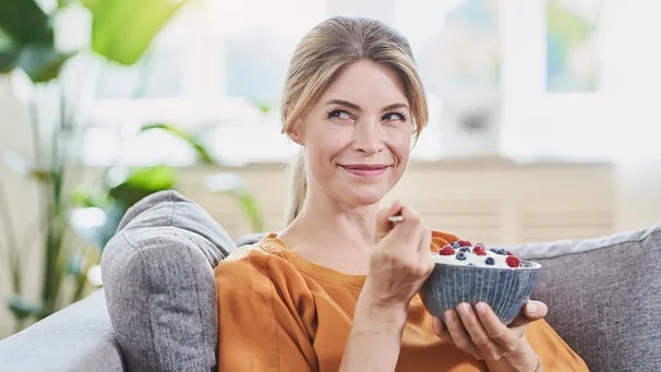 Frau auf dem Sofa isst Joghurt | Bild: mauritius images / Westend61 / Roger Richter