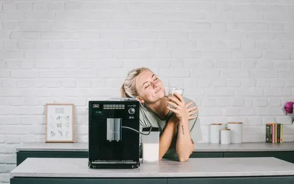 Frau genießt Latte Macchiato, zubereitet mit einem modernen Kaffeevollautomaten mit Milchsystem in einer deutschen Küche.