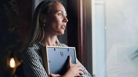 Frau schaut traurig aus dem Fenster und gedenkt des verstorbenen Partners, Thema Rente wegen Todes.